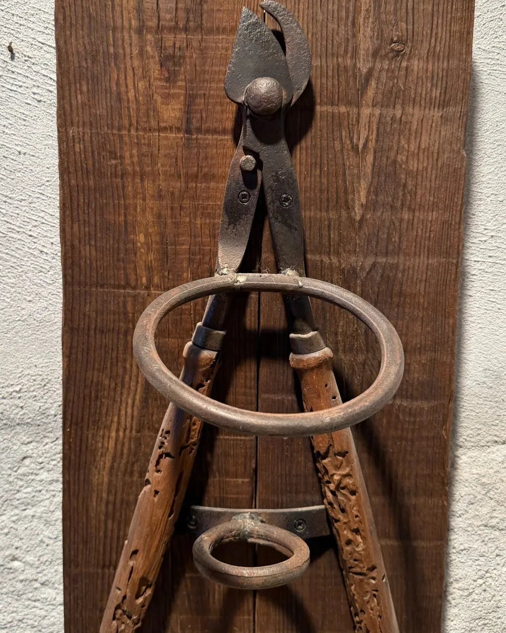 Botellero de pared hecho con unas tenazas antiguas y argollas de hierro sobre una tabla