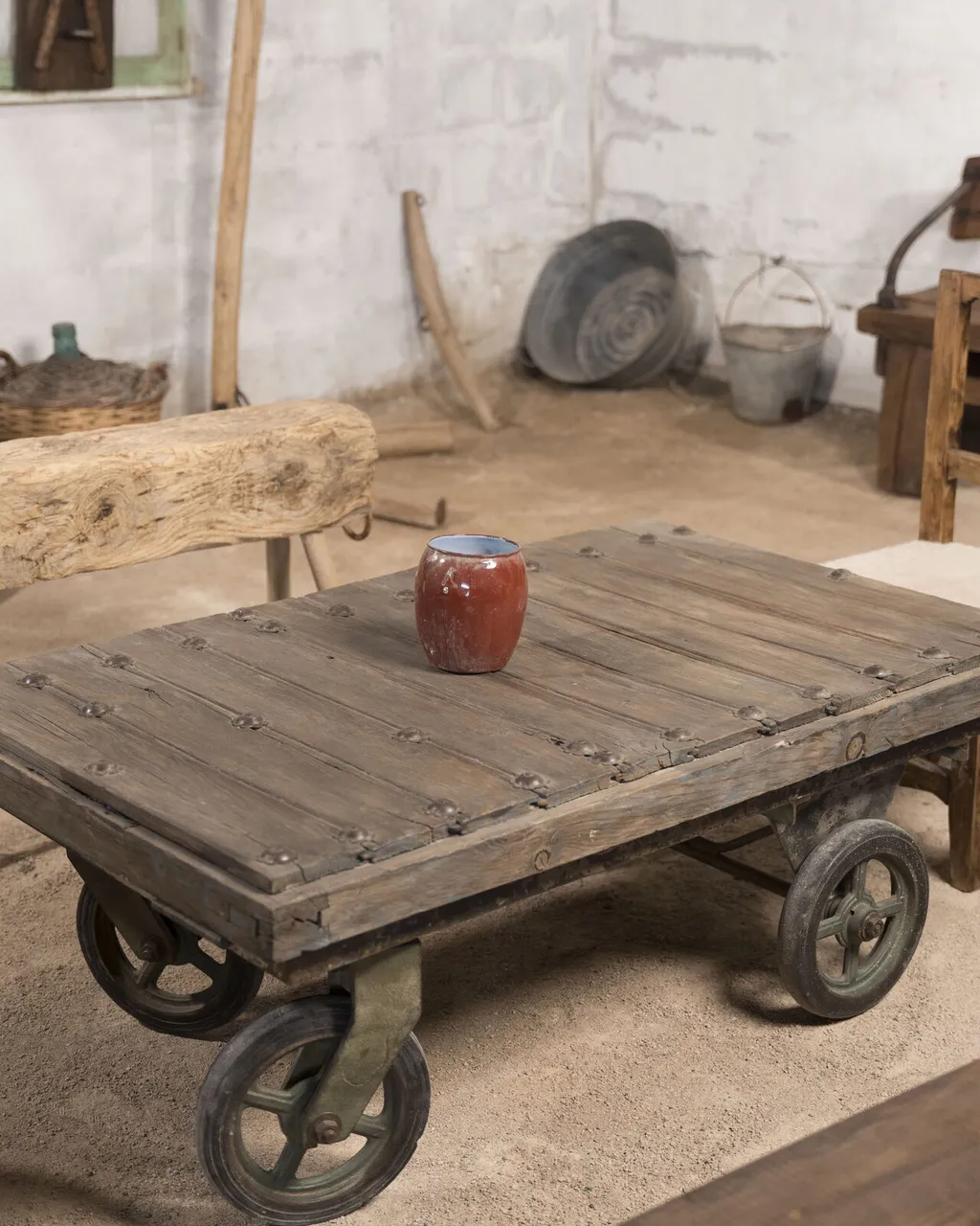 Mesa baja sobre un antiguo carro industrial con ruedas de hierro, con un jarrón rojo encima
