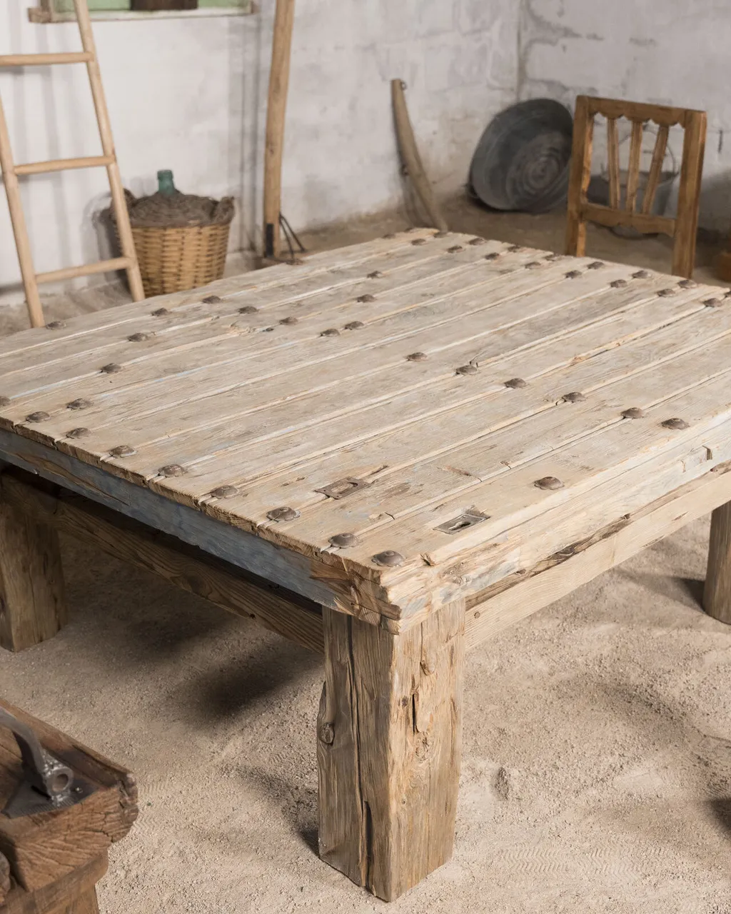 Mesa baja de madera clara con tachuelas de hierro, junto a un taburete de tronco con piel